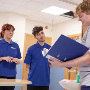 Nurse standing with a clipboard talking to Dundee nursing students at the Clinical Skills Centre