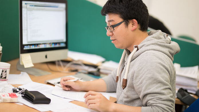 a student working at a desk with paper and a computer