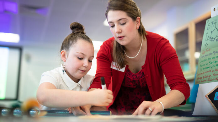 Student teacher with young girl, writing