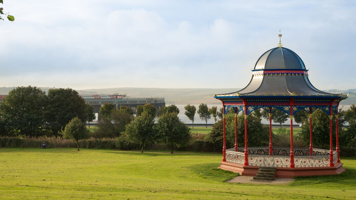 An LNER branded HST with 9 coaches crosses the Tay Bridge with a park and bandstand in the foreground