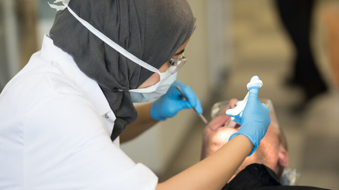 a dental student wearing a mask working on a patients mouth 