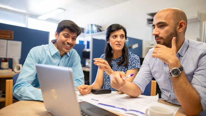 3 people sitting at a desk looking at a laptop