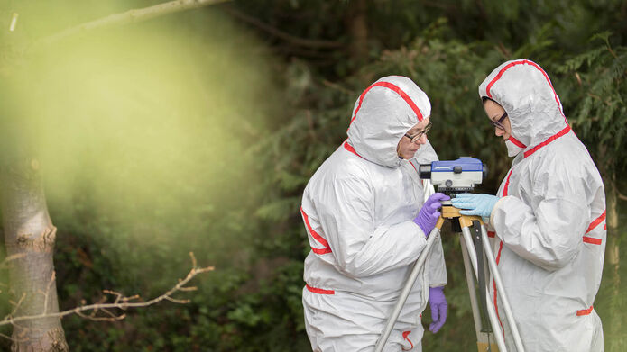 Two forensic scientists set up a camera at a crime scene.