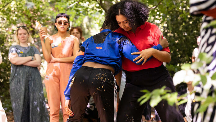 Two people hugging while a group look on set in a garden