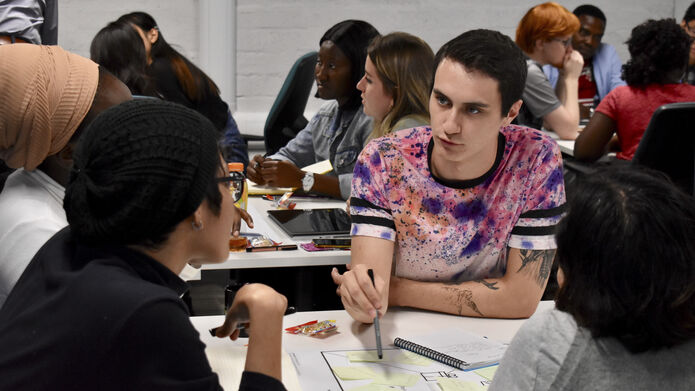 A person talks while pointing to papers on a table in front of other people.