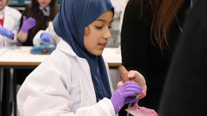 A young girl in a lab coat is looking at a model, held by someone standing up.