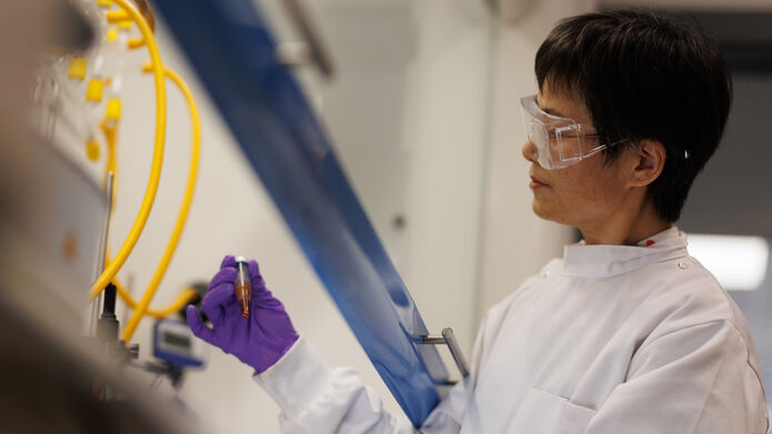 A person wearing purple gloves and goggles in a lab looking at a test tube
