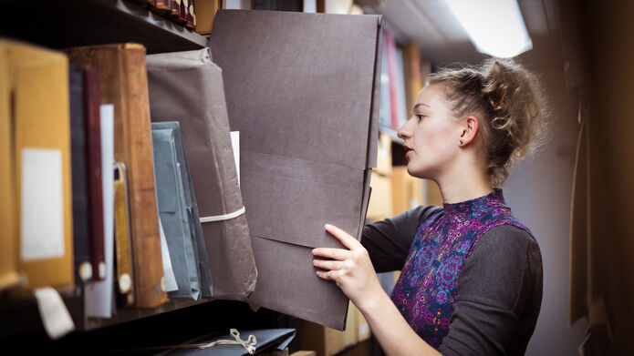 An archivist removes a large folder from off a shelf 