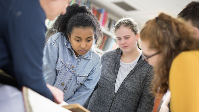 A group of students looking over an old book in Archives
