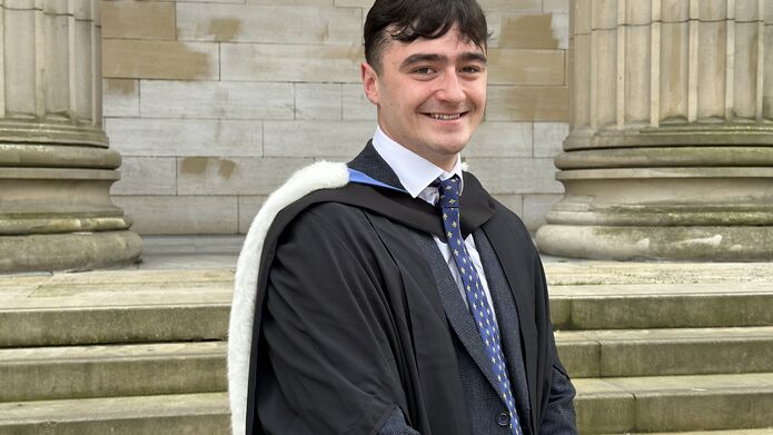 Young male with dark hair wearing graduation gown and hood, with suit and tie underneath