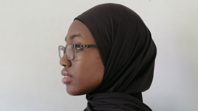 Side profile shot of Hanifah Sogbanmu, who wears a black hijab and glasses