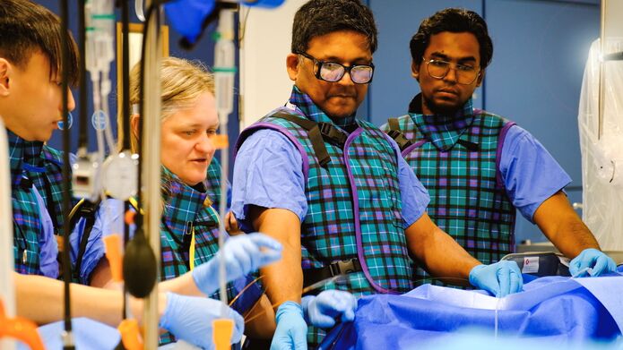 A group of individuals in blue and green uniforms, gathered closely, standing over a table of medical equipment