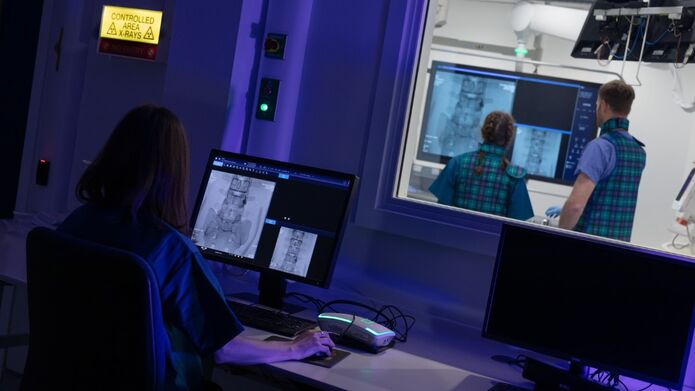 A woman focused on her computer in a dimly lit room in a medical imaging facility with blue lighting