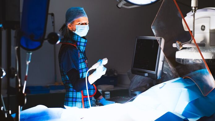 A woman in a blue and green uniform faces the camera whilst holding the controller for ultrasound equipment