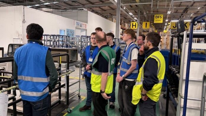 Several people gathered in a factory setting, engaged in conversation near large machines and production equipment