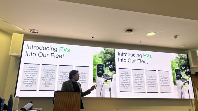 A man gives a presentation in front of a large screen, illustrating key points to the audience