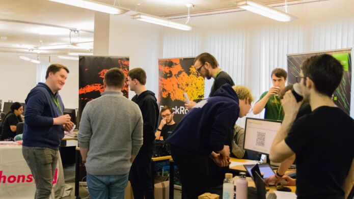 A group of people standing in a circle having a discussion at a hackathon