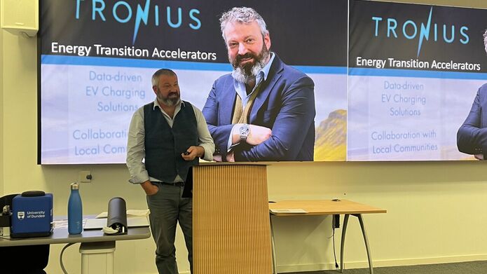 A man stands at a podium, addressing an audience in front of a large presentation screen