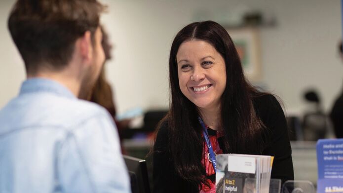 A smiling member of staff in the University's Enquiry Centre speaks to a student, seen from behind