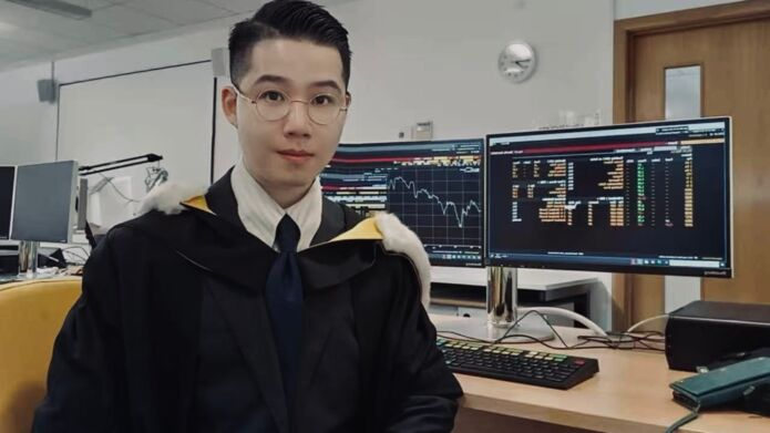 Student sitting infront of a computer, with a graph and statics on the screen, wearing his graduation gown, white shirt and glasses.