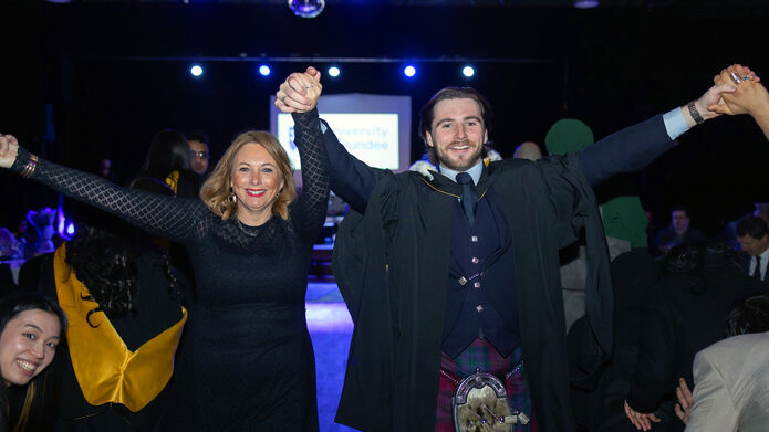 man and woman in graduation robes celebrating inside at a party with raised arms