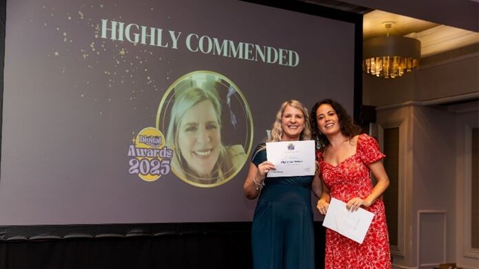 A woman holding up a certificate in front of a screen which says Highly Commended