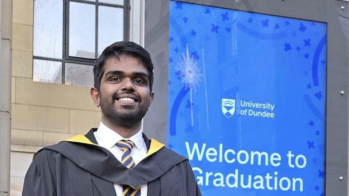 student in front of a welcome to graduation sign