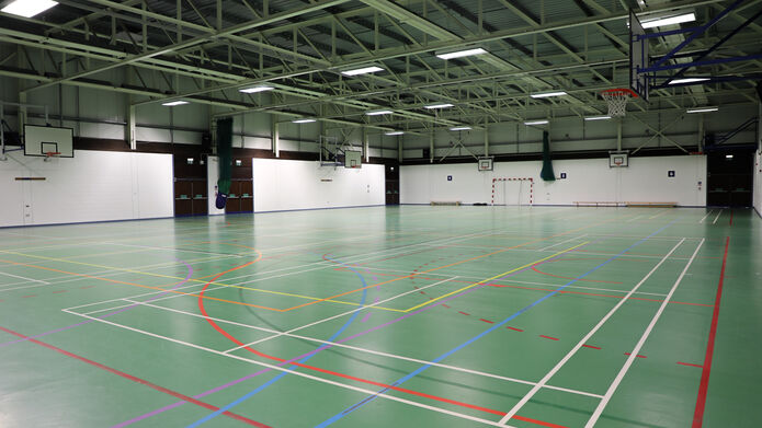 A large sports hall with green flooring with different playing court lines painted on it.