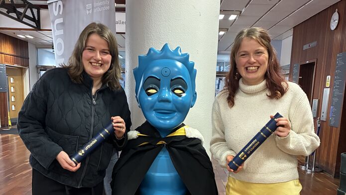 Twins Melissa and Faye Addison pose with graduation scrolls and the Oor Wullie statue in the University of Dundee's Tower Building foyer