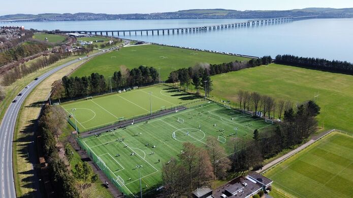 An Aerial view of playing fields beside the River Tay with the rail bridge and the road bridge in the distance.