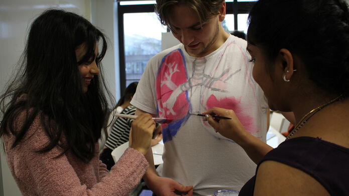 Photograph of two students painting the lungs onto the T-shirt of another student
