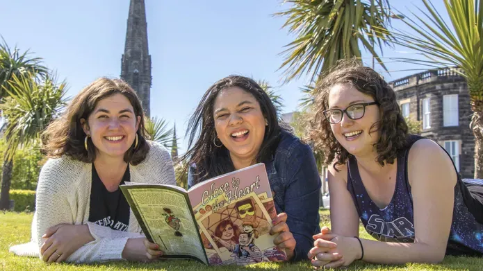 Hailey Austen, Rachel Davis, and Grace Wright outside with one of their comics.
