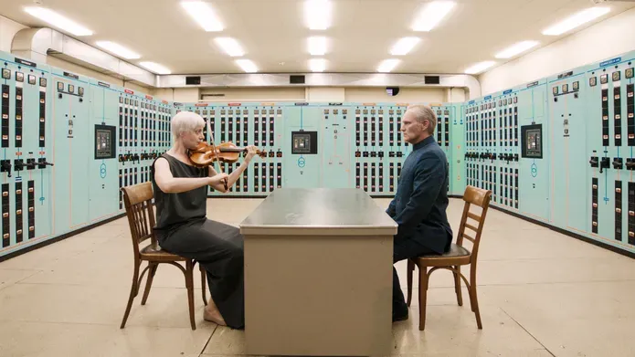 A woman playing a violin while sitting across a table from a man