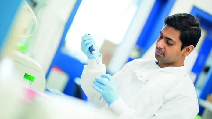 A man in a lab coat with gloves holds a pipet