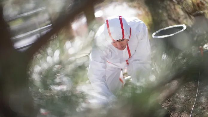 Person in a hazmat suit kneeling on the ground in the woods