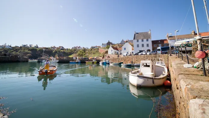 A small fishing boat comes into Crail Harbour, surrounded by buildings from the 17th-19th century
