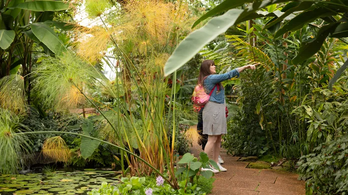 a woman standing pointing at something surrounded by green plants
