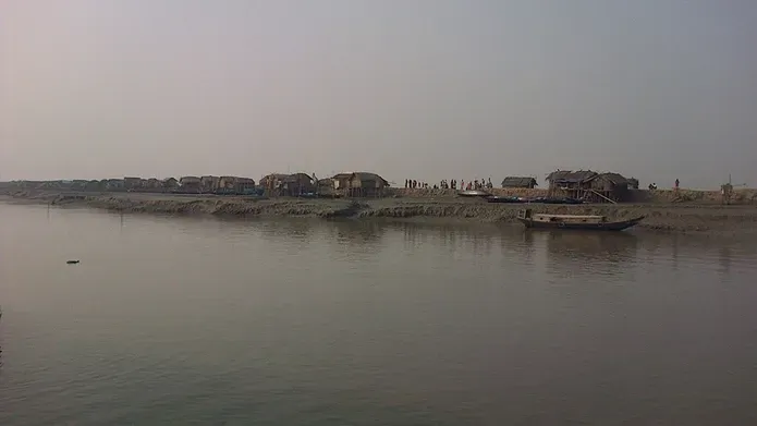 grey looking river with traditional houses alongside it in Bangladesh