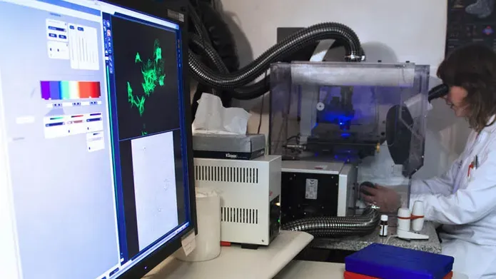 A person in PPE looking through a microscope