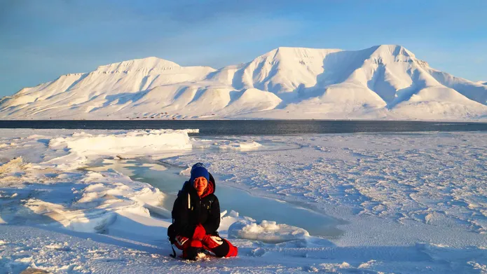 a person sitting on the snow with snow covered mountains in the background
