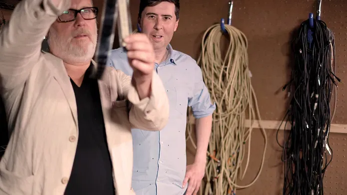 2 men examining something with ropes hanging on the wall behind them 