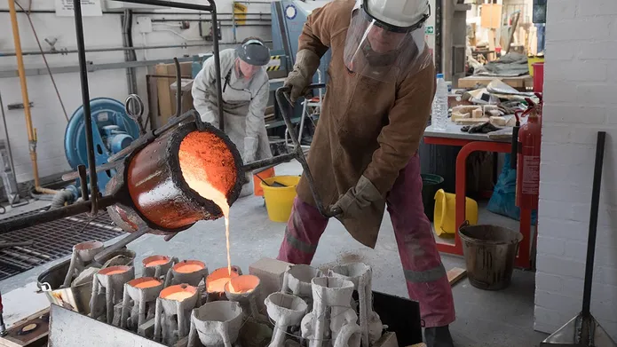 a person in protective gear pouring molten metal into moulds