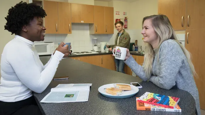 Students eating and drinking around kitchen table