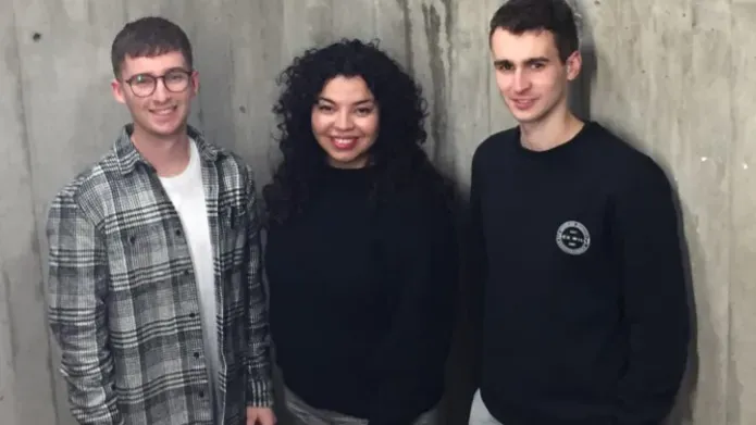Three students standing before a concrete wall