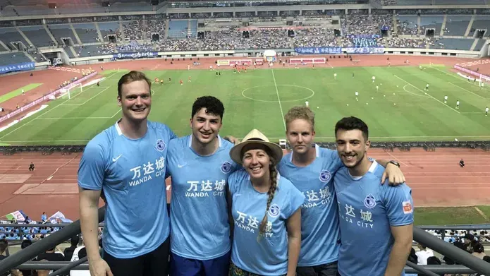 5 people in blue football kits with a footfall stadium behind them 