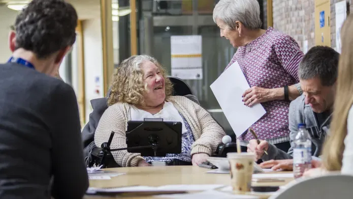 Female User Centre participant who uses communication device for speaking in conversation with volunteer during a group session.