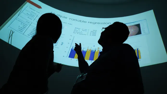 two people in shadow pointing at a large projected computer screen with a graph on it