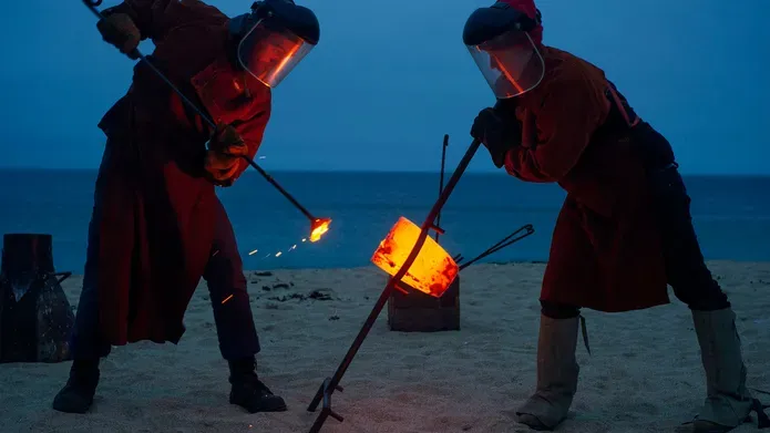 people on beach with sticks with molten metal on the end for bell casting