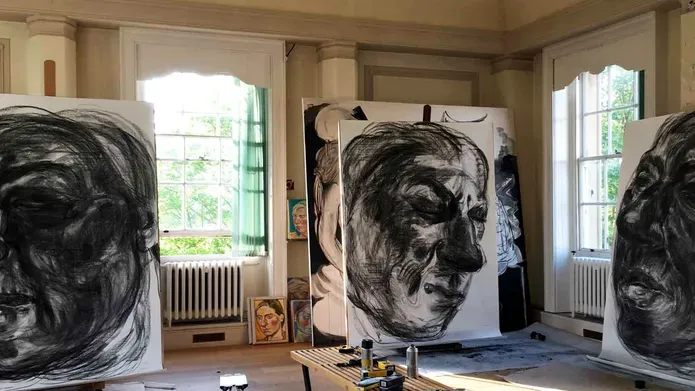 Canvases with heads painted on them, stacked up around a bright gallery