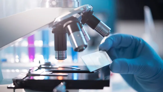 a close shot of a microscope with a gloved hand holding a glass slide